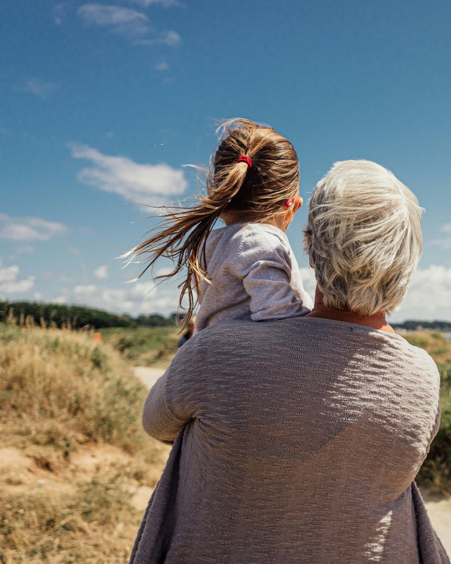 Une grand-mère portant sa petite-fille dans les bras, face aux dunes